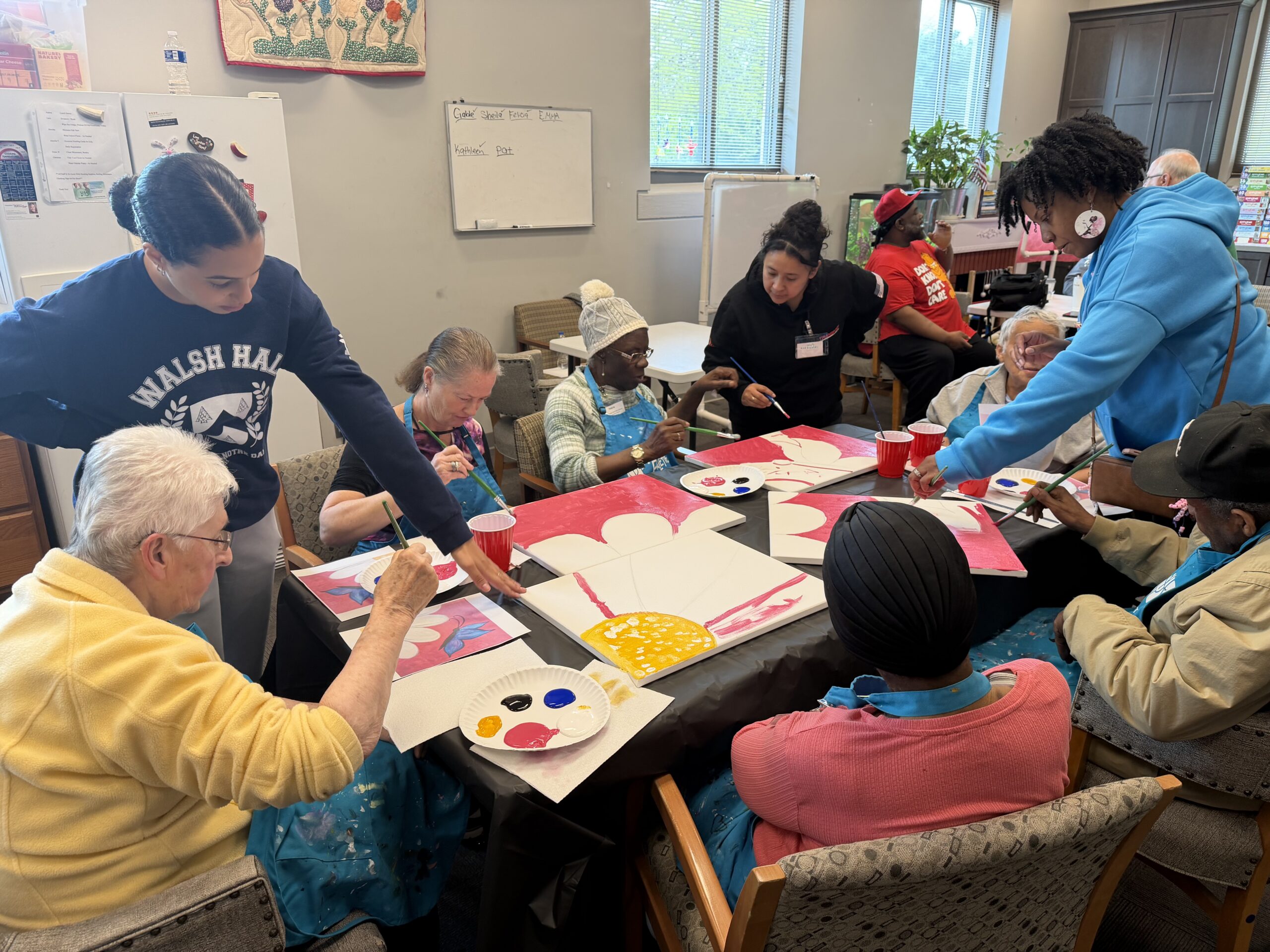 A diverse group of people sitting around a table painting on canvases with small brushes and paint palettes.