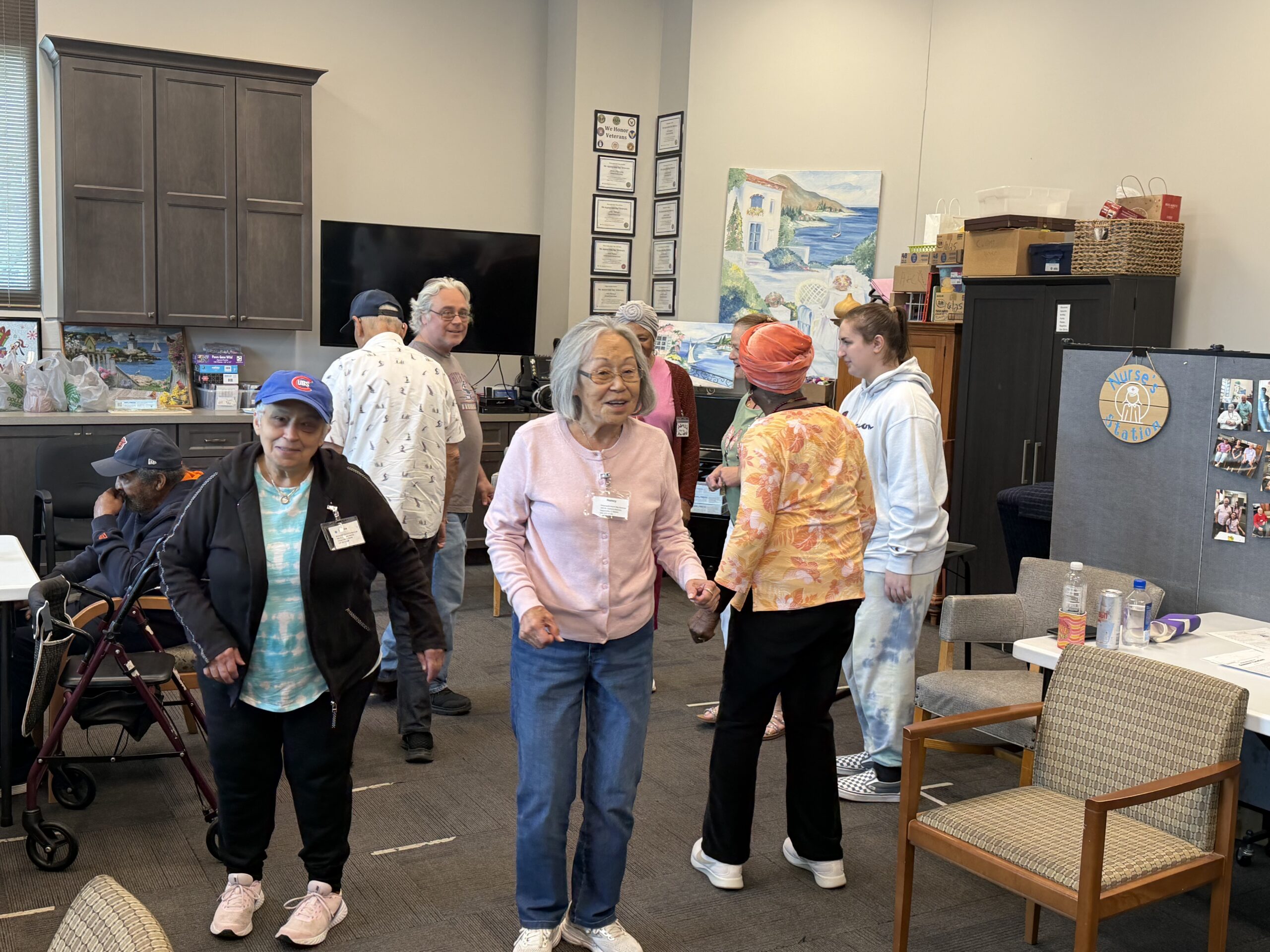 A diverse group of seniors participate in a social gathering or light exercise class in a community room.
